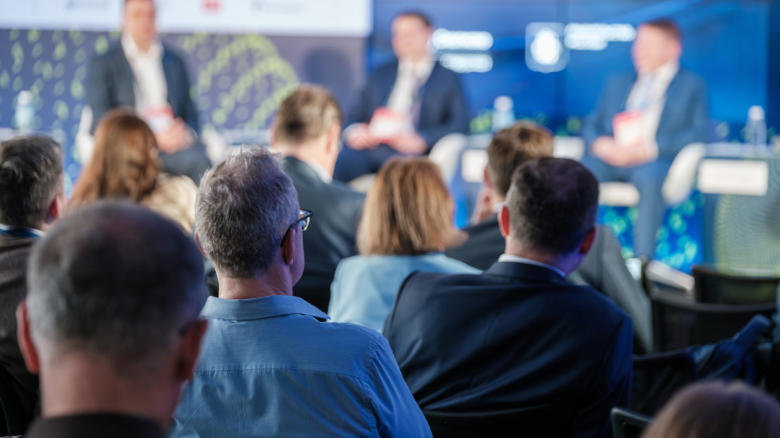Audience attentively watching a business panel discussion during a professional conference. Engaged participants viewing speakers on stage.